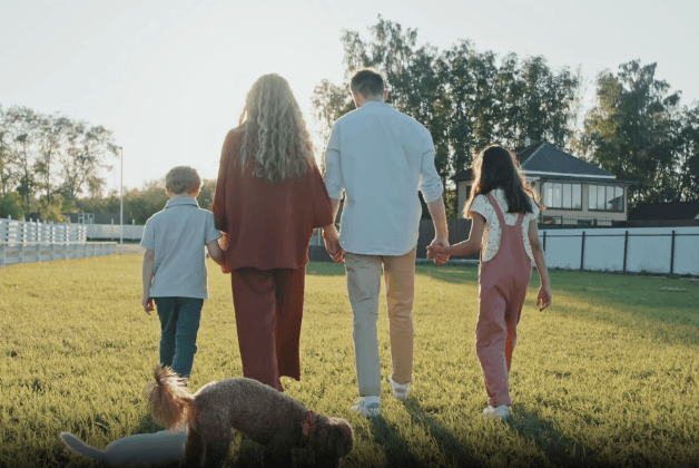 A family walking together across a grassy backyard, holding hands