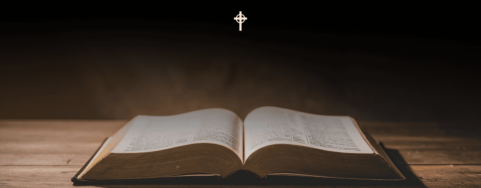 An open Bible on a wooden table beneath a glowing cross